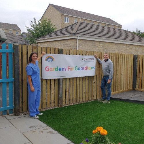 Two residents holding up a multicoloured gardens for guardians banner over a wooden fence